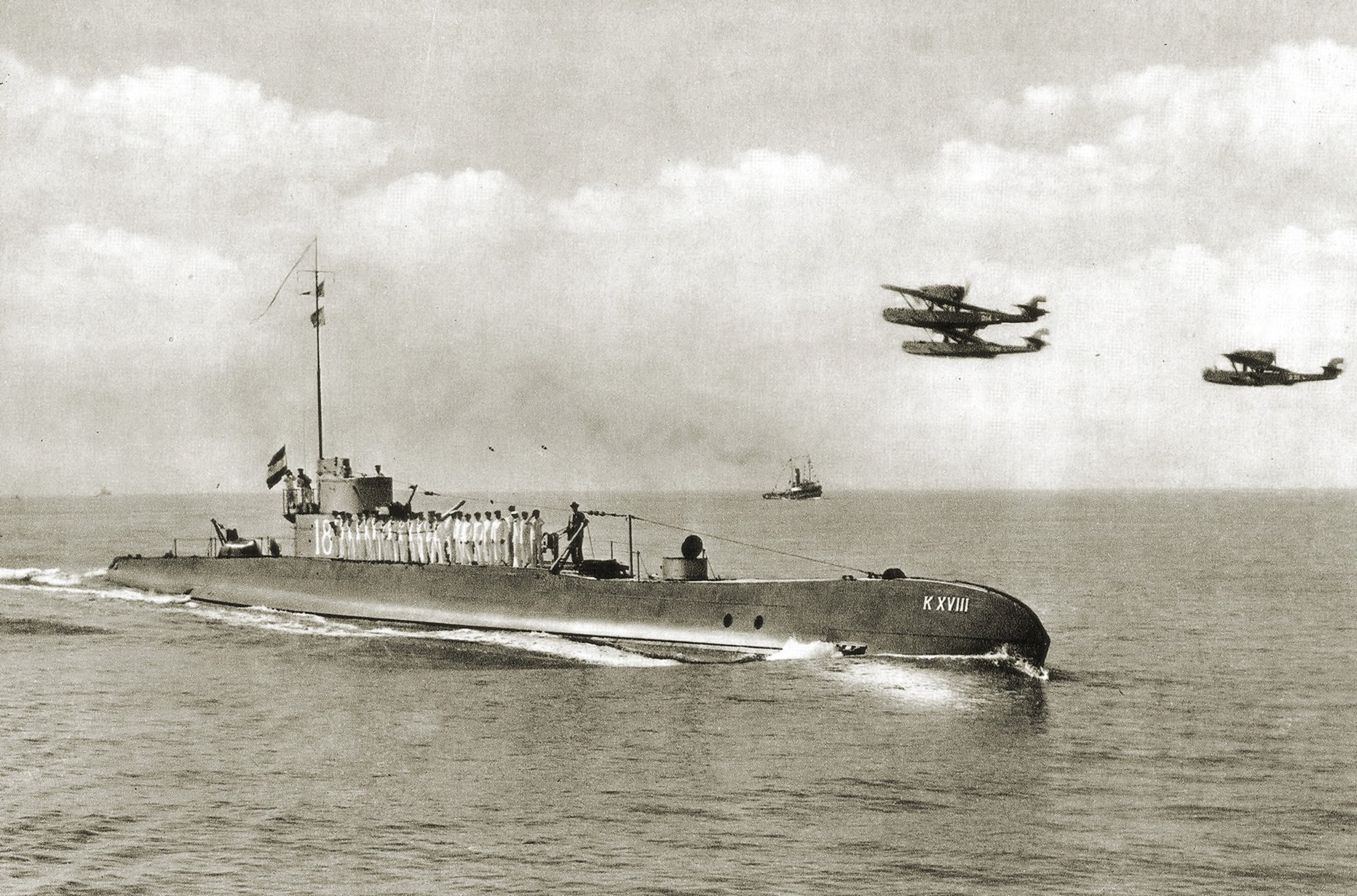 Hr.Ms. K 18 bij binnenkomst in Soerabaja, 1935. In de lucht vliegen drie Dornier Do J-Wal vliegboten (foto: collectie NIMH)