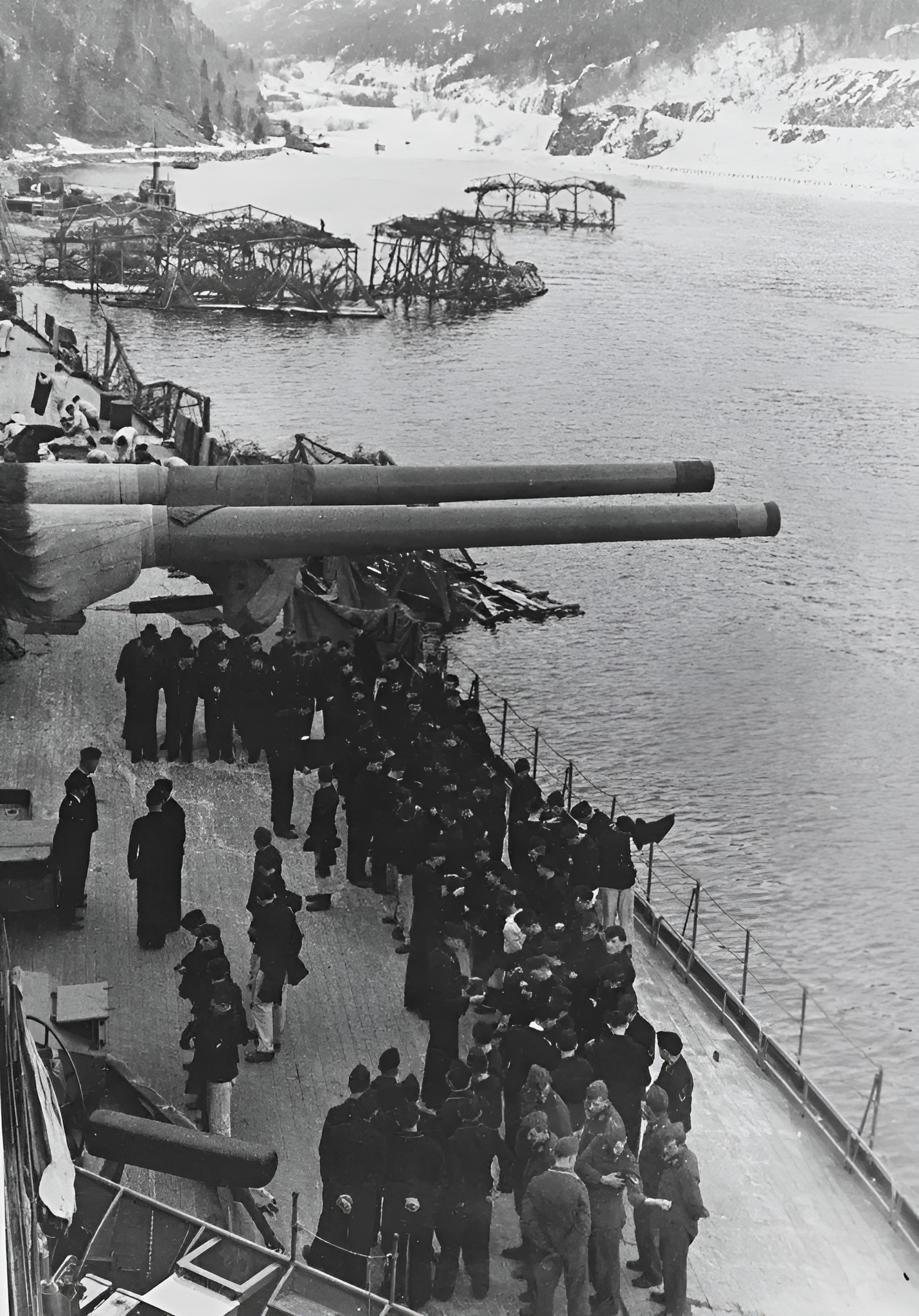 Het Duitse slagschip Tirpitz ligt afgemeerd in een Noors fjord. Bemanningsleden, onder hen Nederlanders, begeven zich aan dek (bron: Wikimedia Commons)