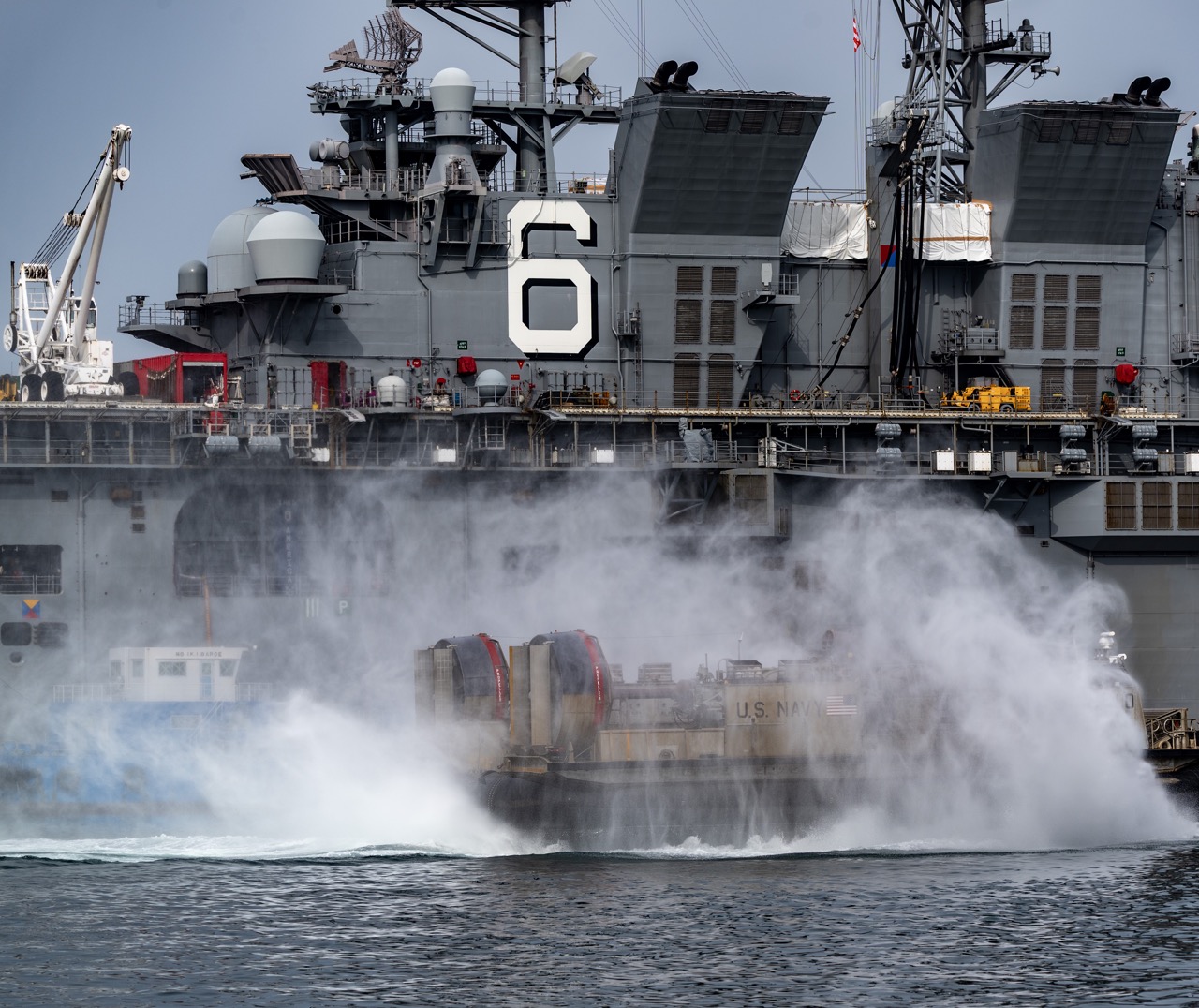 A Landing Craft Air Cushion (LCAC) assigned to Naval Beach Unit (NBU) 7 transits the Juliet Basin alongside the forward-deployed amphibious assault ship USS America (LHA 6) at Commander, Fleet Activities Sasebo (CFAS) in support of the Sasebo Fleet Friendship Day open-base event April 5, 2025. CFAS opened its main base complex to the public to celebrate the friendship and partnership between the U.S. Navy, Japan Self-Defense Forces (JSDF), and the local Japanese community. (U.S. Navy photo by Mass Communication Specialist 1st Class Kristen Yarber)